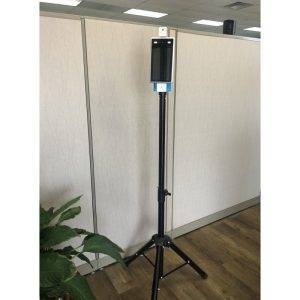 An adjustable tripod mount with a display screen stands in an office setting next to a plant.