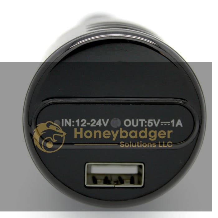 Close-up view of a black USB car charger showing input and output specifications: IN: 12-24V OUT: 5V---1A.