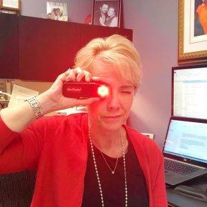 A woman holds a Spy Finder Pro up to her eye, examining it as it emits a bright red light.