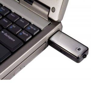 A close-up view of a laptop keyboard with an 8GB USB Flash Drive Voice Recorder connected to it.