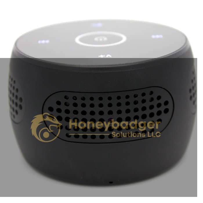 A small, round black Bluetooth speaker with perforated grills and touch control buttons for discreet surveillance.