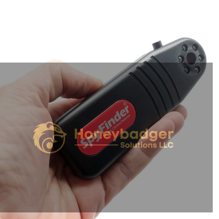 A hand holding the Spy Finder Pro, a black device used to detect hidden cameras, featuring a red label and multiple lights around a central lens.