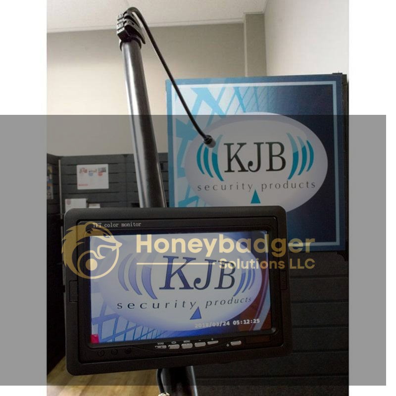 A monitor displaying the KJB Security Products logo, positioned in an office setting.