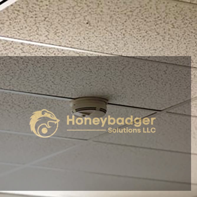 Smoke detector installed on a white drop ceiling with speckled acoustic tiles.