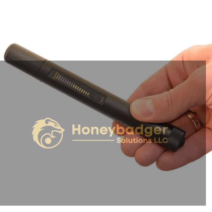 A hand holds a Detection and Counter Surveillance Kit, a black cylindrical device with a slider and indicator lights.