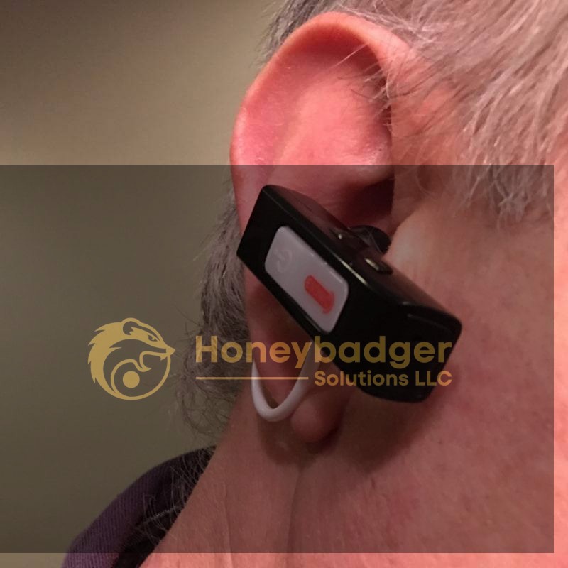 Close-up of a person's ear wearing a Mini Voice Amplifier, a black Bluetooth earpiece with a white and red button.