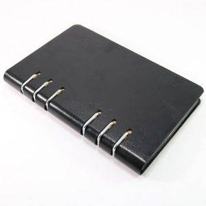 A black leather-bound notebook with four metal ring bindings on a white surface.