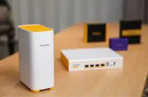 A white Firewalla Access Point 7 with yellow accents on a wooden table beside a white network device.