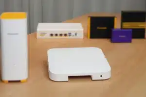 A Panasonic network device with a white body and yellow accents placed on a wooden table with other devices in the background.