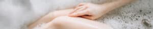 Close-up of a person's hands resting on their knees in a bath filled with bubbles.