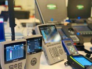 Close-up of multiple handheld electronic devices with digital displays and controls arranged on a table in a tech workspace.
