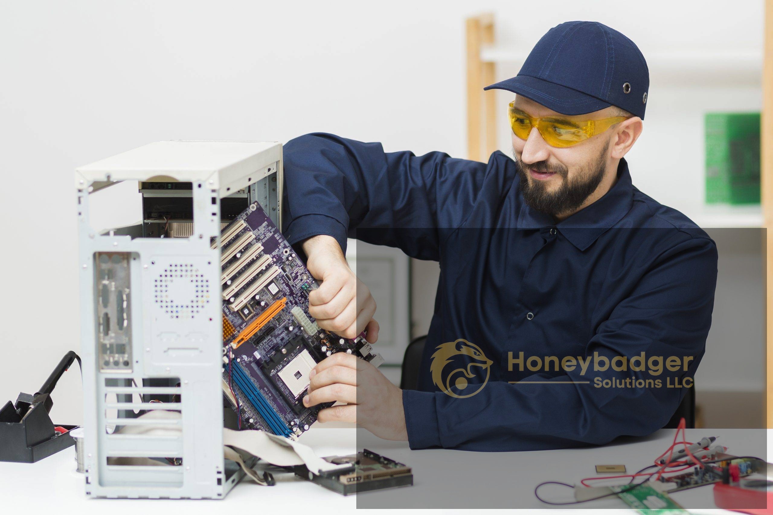A technician in a navy cap and yellow safety glasses is working on a motherboard inside an open computer case.