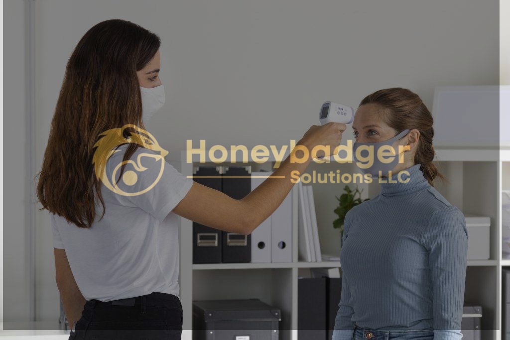 A woman in a white mask checks another woman's temperature with a handheld infrared thermometer while both wear face masks.