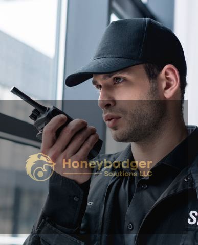 Security guard in a black uniform communicating via a walkie talkie while standing indoors.