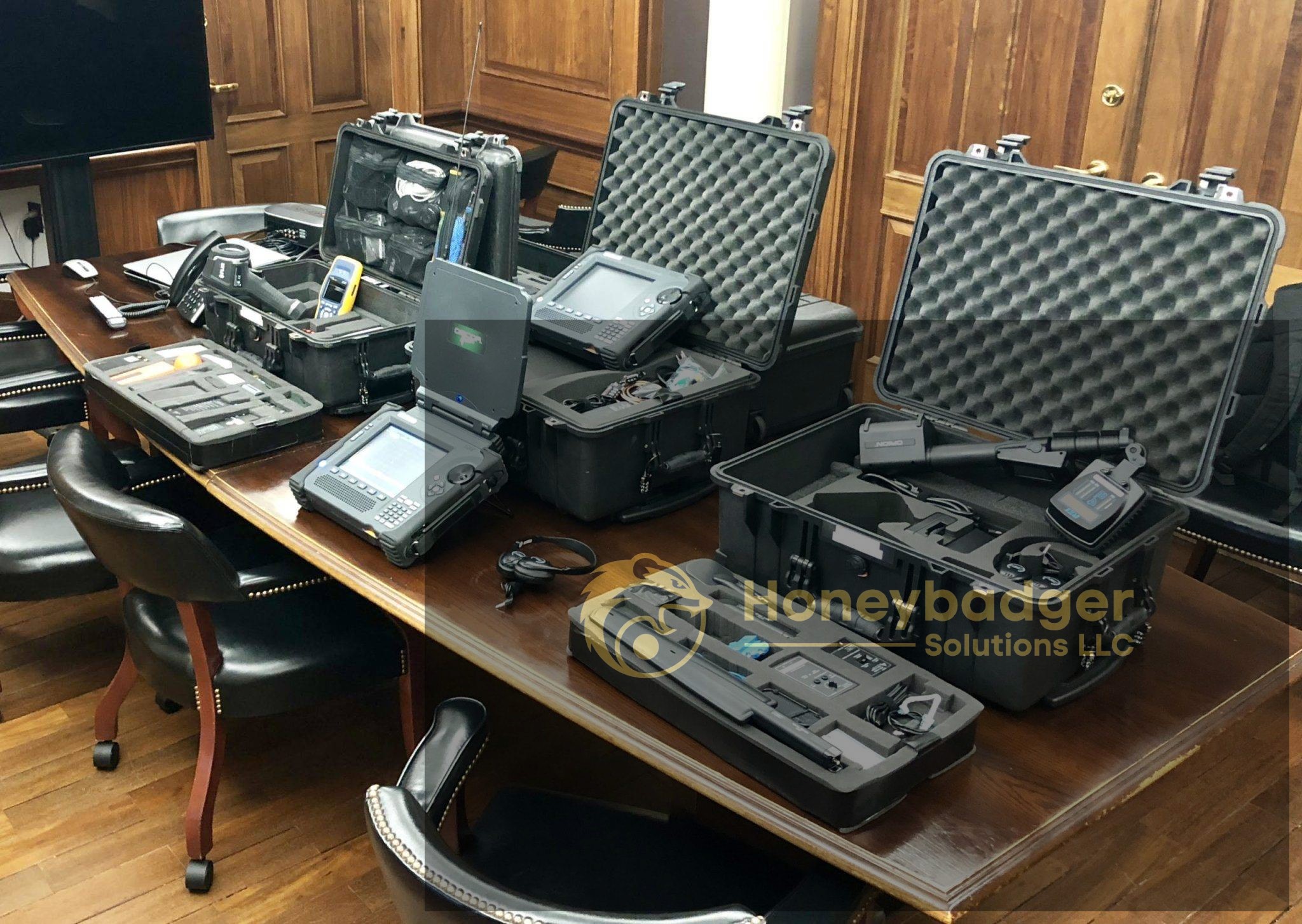 Multiple equipment cases with open lids displayed on a wooden table in a meeting room.
