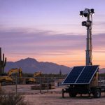 Remote video monitoring camera tower with talk-down speaker guarding an Arizona construction yard at dusk