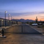 Self storage security at an Arizona facility: gated entry, lit drive aisle and rows of roll-up units at dusk