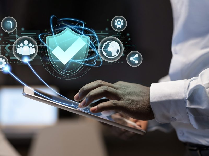 A person in a white shirt uses a tablet with digital security icons, such as a shield and gears, floating above—symbolizing cybersecurity and data protection vital for digital forensics and financial investigations.